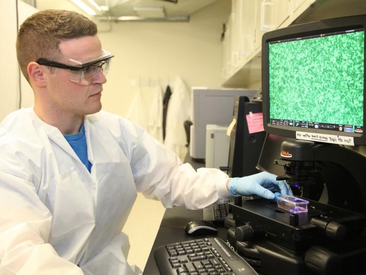 A student wearing 安全 glasses and white coat studies lab project on laptop